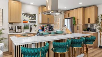 A modern kitchen with a central island, bar stools, wooden cabinets, and a stainless steel refrigerator.
