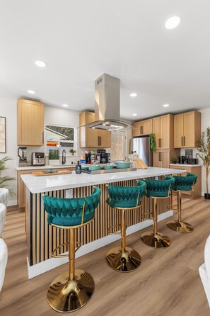 A modern kitchen with a central island, bar stools, wooden cabinets, and a stainless steel refrigerator.