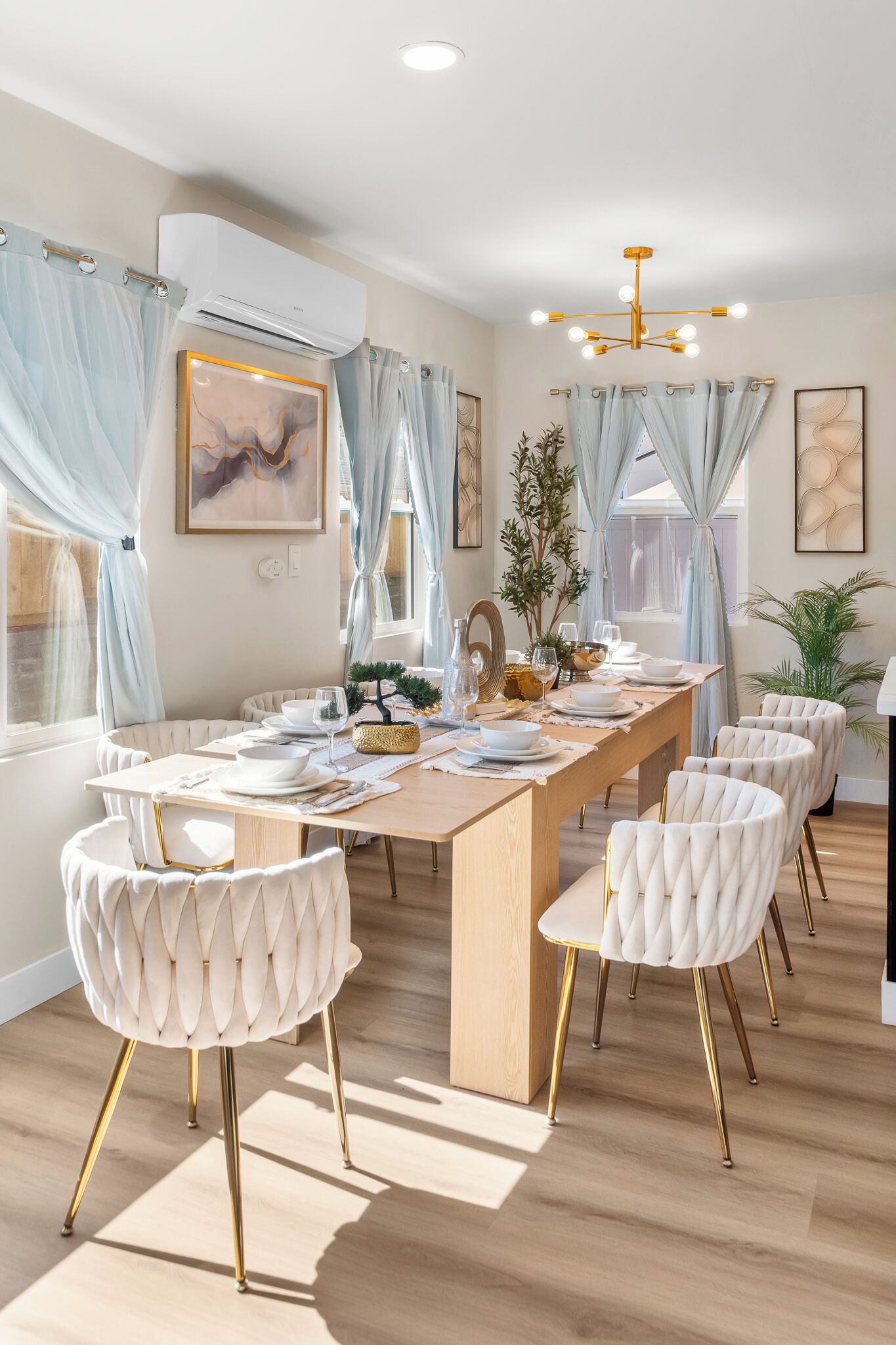Een eetgedeelte met een lange tafel, beklede witte stoelen en een kroonluchter.