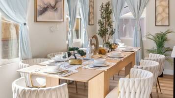 Een eetgedeelte met een lange tafel, beklede witte stoelen en een kroonluchter.