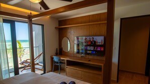 Ett hotellrum med en säng, ett skrivbord med en tv, en stol och utsikt över stranden.