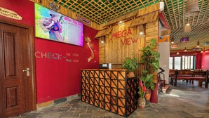 Un espace d’accueil avec un comptoir de réception en bois, un grand écran affichant un menu et un panneau indiquant le comptoir d’enregistrement.