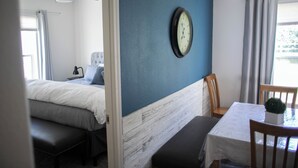 Et soveværelse med seng, sengebord, stol, et lille bord med en plante og et vægur.