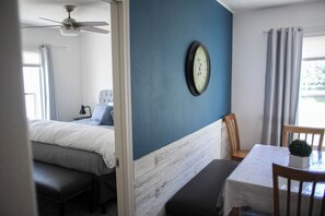A bedroom with a bed, a bedside table, a chair, a small table with a plant, and a wall clock. - Fantastic Cedar Lane Cottage, walking distance to beach and sports park (Garden City)