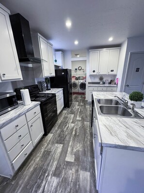 A modern kitchen with white cabinetry, a black stove, and a marble countertop. - Fantastic Cedar Lane Cottage, walking distance to beach and sports park (Garden City)