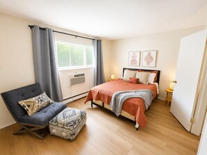 A bedroom with a bed, a chair, a small table, and a window with curtains. - Newly Remodeled + Modern Aztec Themed + 1 Bed/1 Bath Near Airport (Lansing)