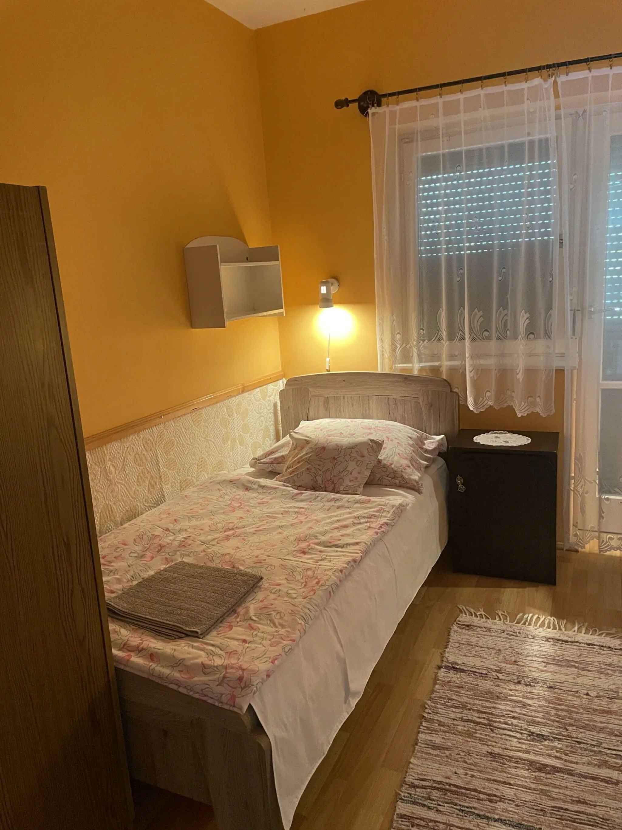 Un dormitorio con cama, mesita de noche, lámpara y ventana con cortinas.