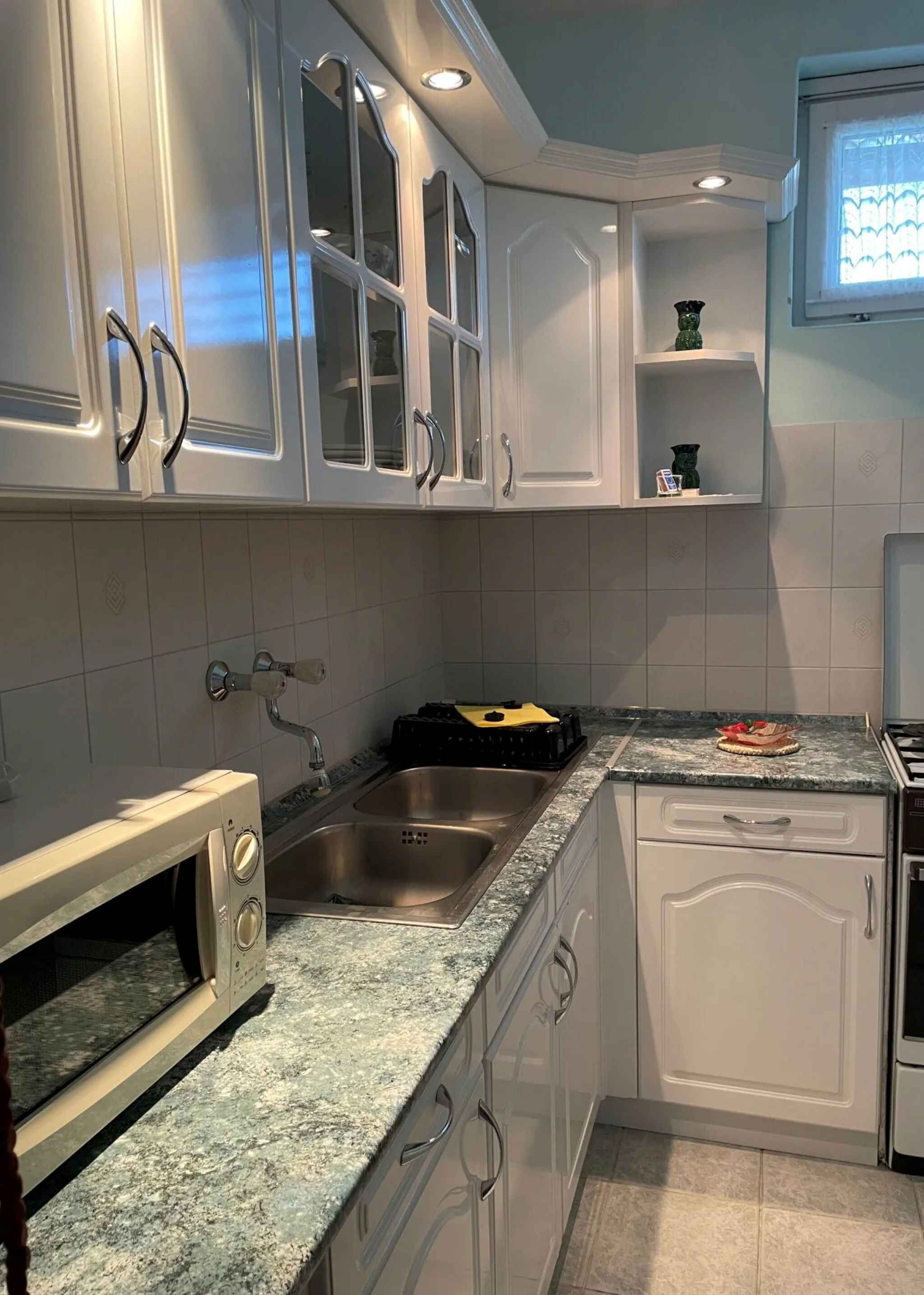 Uma cozinha com armários brancos, uma pia dupla, um micro-ondas e um balcão com escorredor de louça.
