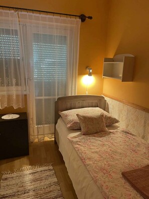 A bedroom with a bed, a bedside table, a lamp, a window with curtains, and a wall-mounted shelf. - Holiday home with large garden, garden pavilion and barbecue (Zalakaros)