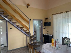 A room with a wooden staircase, a television mounted on the wall, a table with a vase of flowers, and a clock. - Holiday home with large garden, garden pavilion and barbecue (Zalakaros)