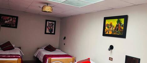 Une chambre avec deux lits, un luminaire au plafond et des œuvres d’art accrochées au mur.