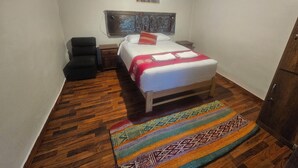 Un dormitorio con cama, mesita de noche, una silla, armario de madera y una alfombra estampada.