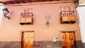 Un edificio con dos puertas de madera, un balcón con barandilla y un cartel sobre las puertas.