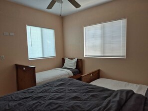 Ein Schlafzimmer mit zwei Betten, einem Deckenventilator und zwei Fenstern mit Jalousien.