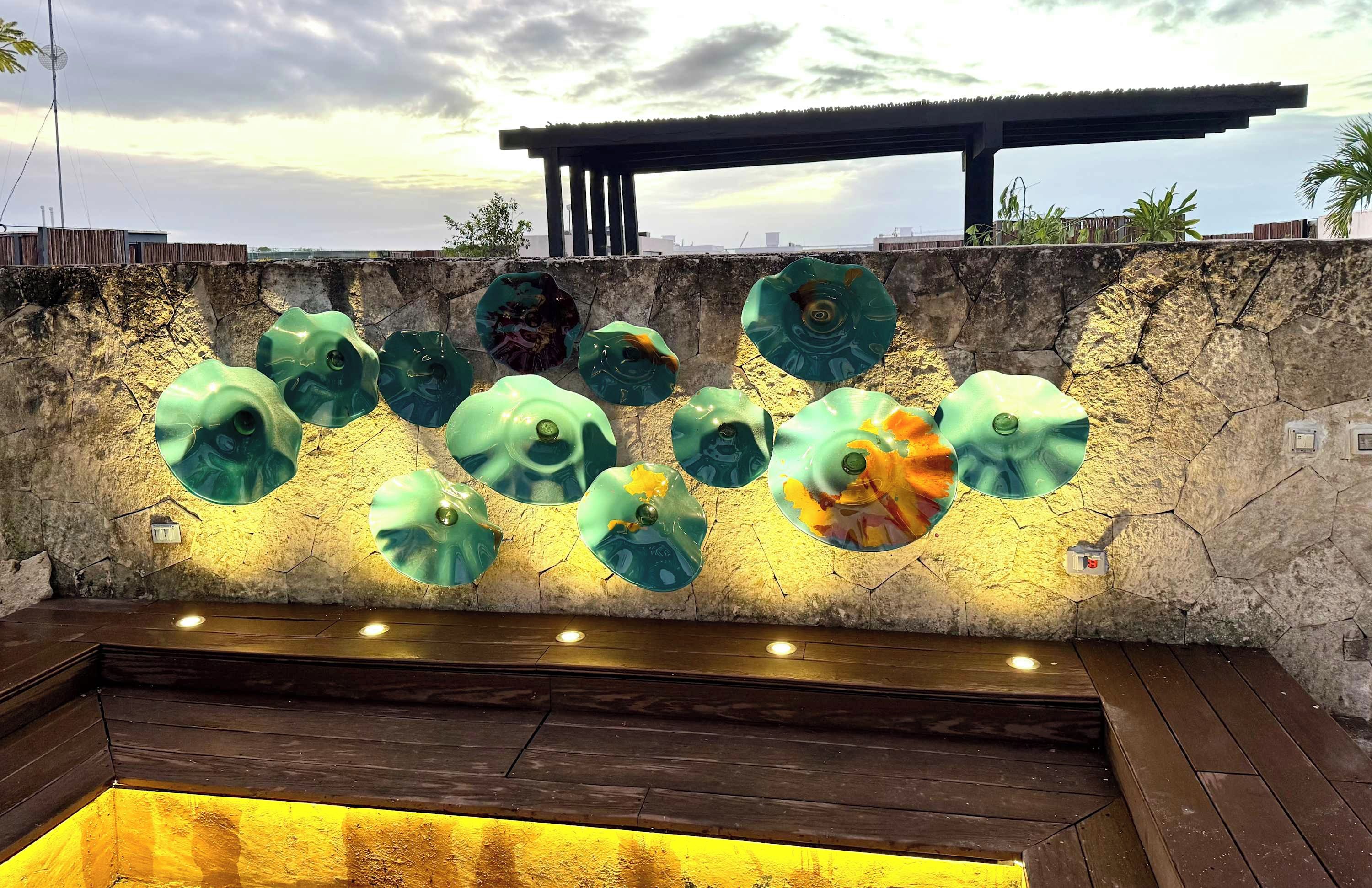 A pool area with a stone wall and multiple green glass sculptures.