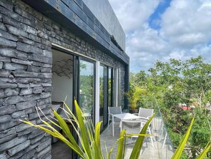 A modern building with a stone facade, a glass door entrance, and a patio with outdoor furniture. - Black House - Modern 3BR Villa with Private Pool (Tulum)