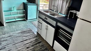 A compact kitchen with a built-in oven, a sink, and a small refrigerator. There is a shelf unit with decorative items and a rug on the floor. - Cozy lil 1 bedroom getaway (Rockport)