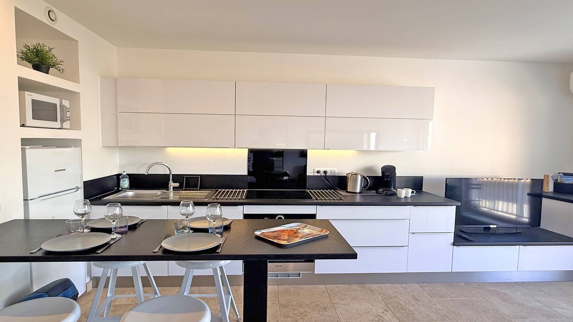 A modern kitchen with white cabinets, a black countertop, and a dining area with white chairs.