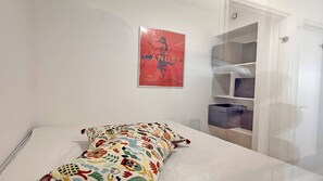 Ein Schlafzimmer mit Bett, einem farbenfrohen Kissen, einem Bild an der Wand und einem Kleiderschrank.