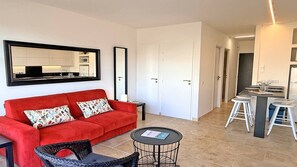Ein gemütlicher Wohnbereich mit einem roten Sofa, einem runden Tisch, einem schwarzen Stuhl und einer Küchenzeile mit Esstisch.