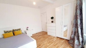 Ein Schlafzimmer mit einem Bett, einem Kleiderschrank, einem kleinen Tisch mit Pflanze und einem Vorhang.