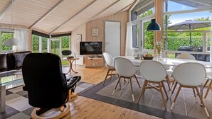 A spacious living area with a high ceiling, a television, a dining table with chairs, and large windows offering a view of greenery. - "Ljubinko" - 300m from the sea by Interhome (Sydals)