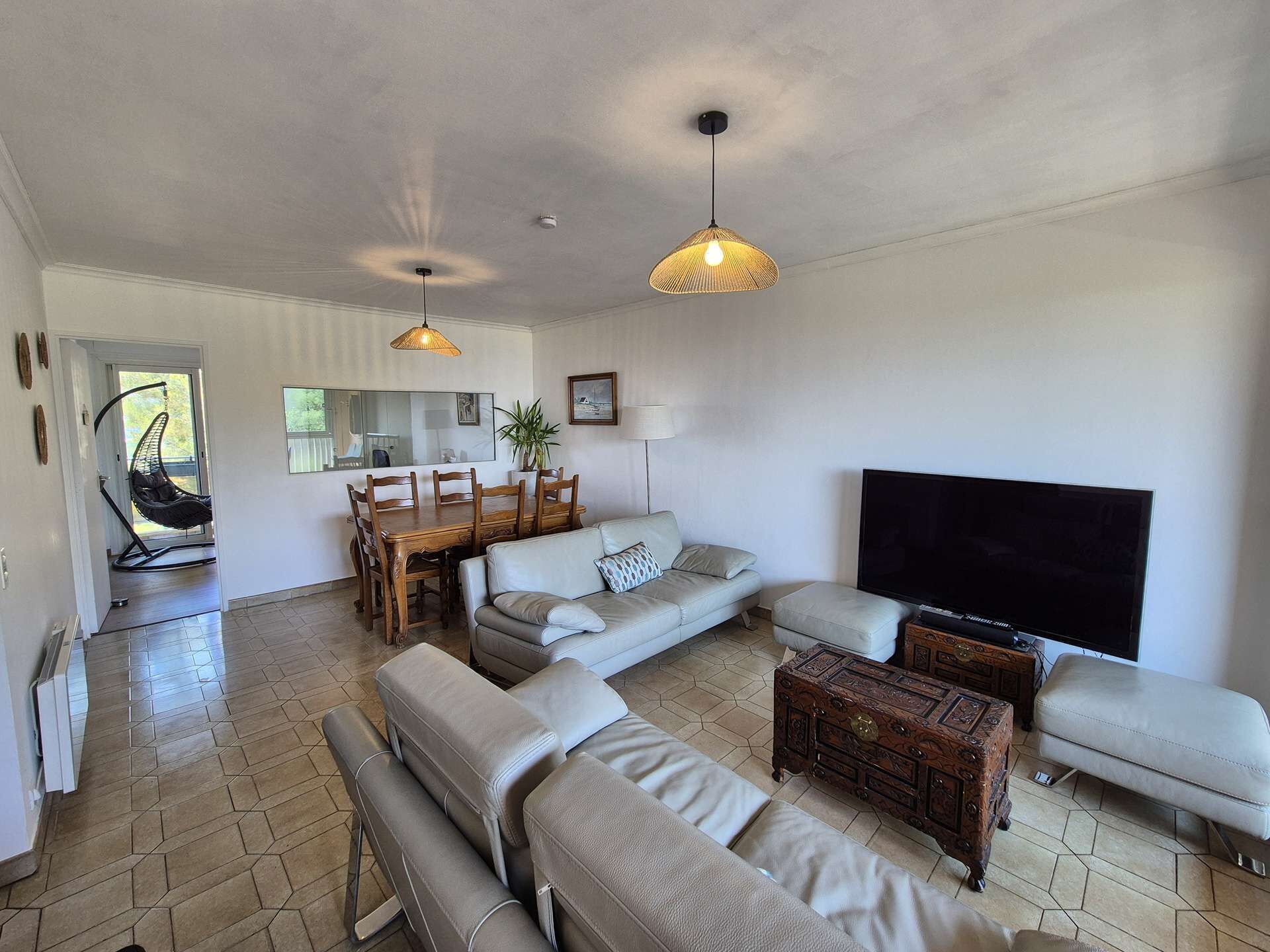 A living room with a sofa, ottoman, coffee table, TV, dining table, chairs, hanging light fixture, and a hanging chair.