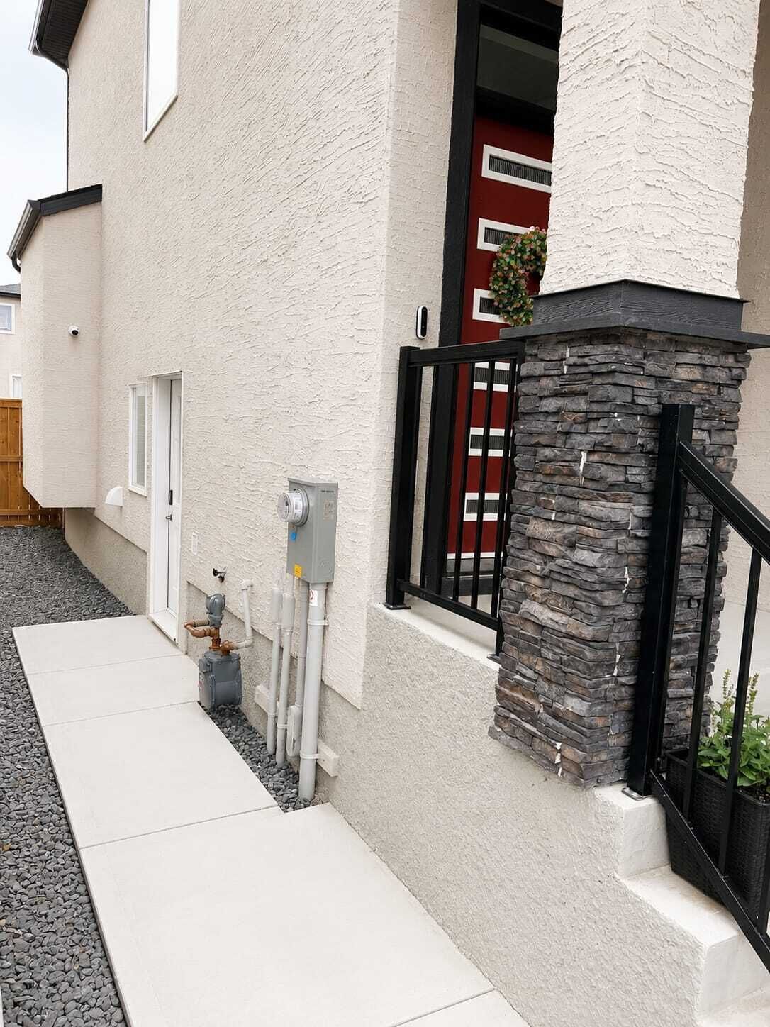 Un bâtiment moderne avec une façade en pierre, un portail en métal noir et une porte rouge.
