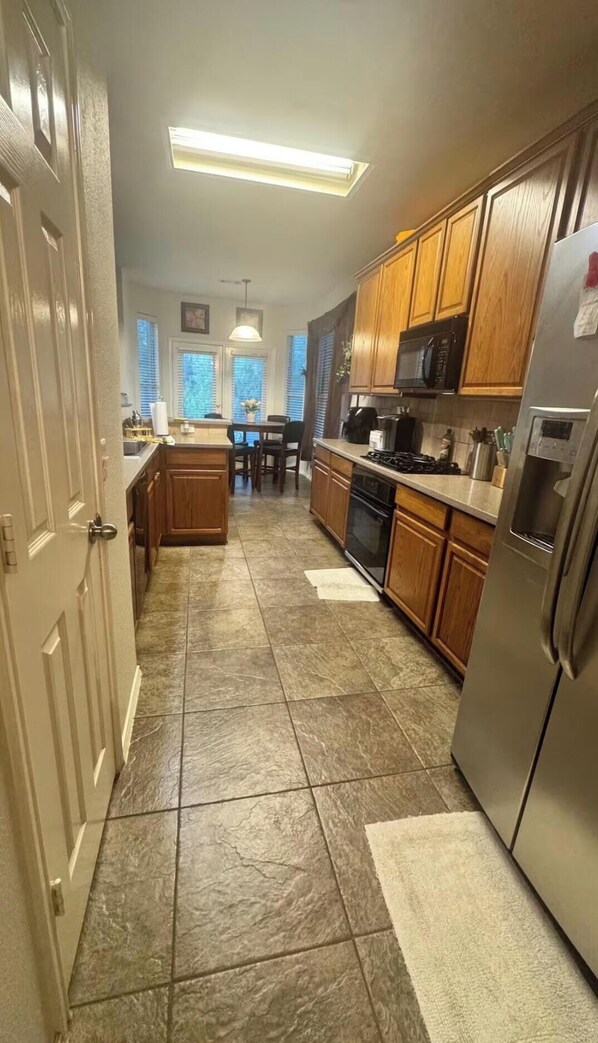 A kitchen with wooden cabinets, a stainless steel refrigerator, and a tiled floor. - Cozy 3-bedroom house in perfect Grand Prairie with AC (Grand Prairie)