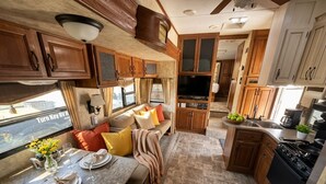 Een compact camperinterieur met een eethoek, kitchenette en een leefruimte met een bank en kussens.