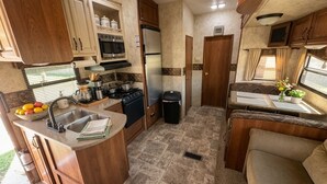 Een kleine camperkeuken met een spoelbak, fornuis, magnetron en koelkast.