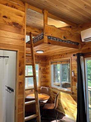 A wooden cabin interior with a loft bed, a dining table with chairs, and a ladder to the loft. - Mountain View Treehouse in Sutherlin with full bath and AC, 5 minutes from I-5 (Sutherlin)