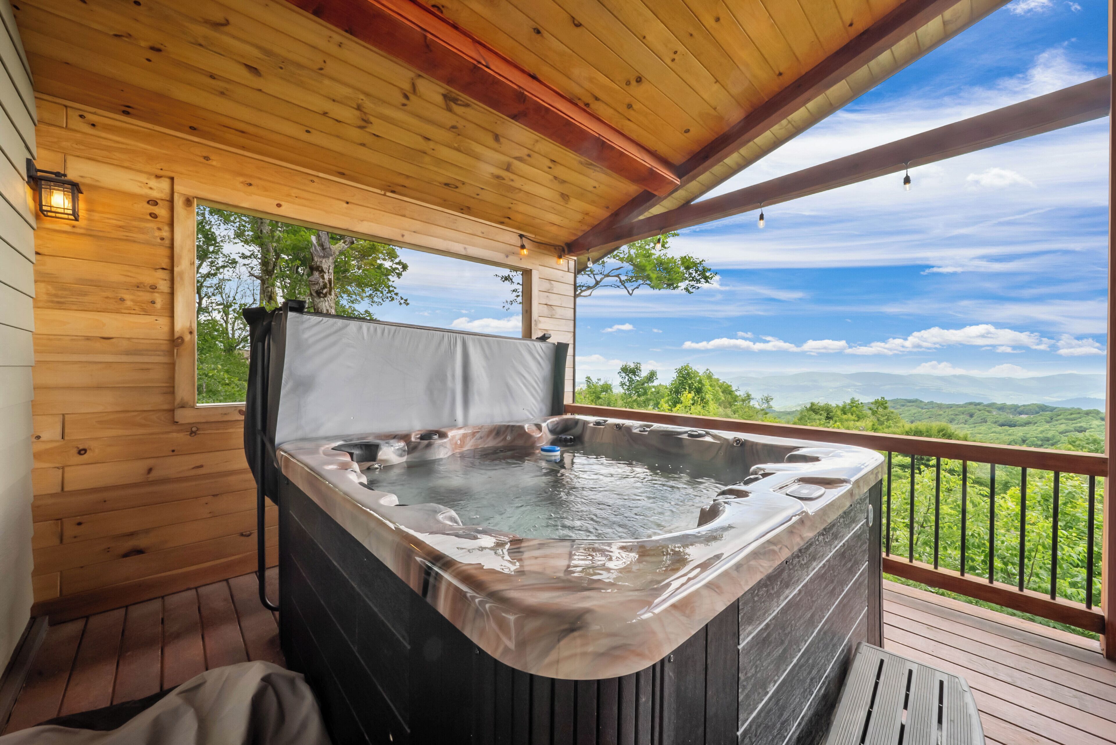 Un bain à remous sur une terrasse en bois, avec vue sur une forêt et des montagnes.