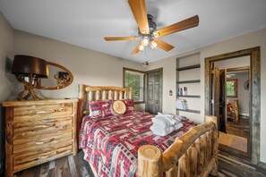 Ein Schlafzimmer mit einem hölzernen Bett, einem Deckenventilator, einer Kommode und einem Spiegel mit einer Hirschdarstellung.