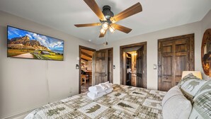 Ein Schlafzimmer mit einem Bett, einem Deckenventilator, einem Gemälde und Holztüren.