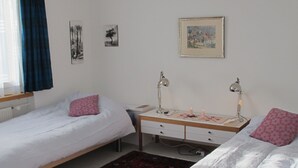 Un dormitorio con dos camas individuales, un escritorio con silla, un radiador y una ventana con cortinas.