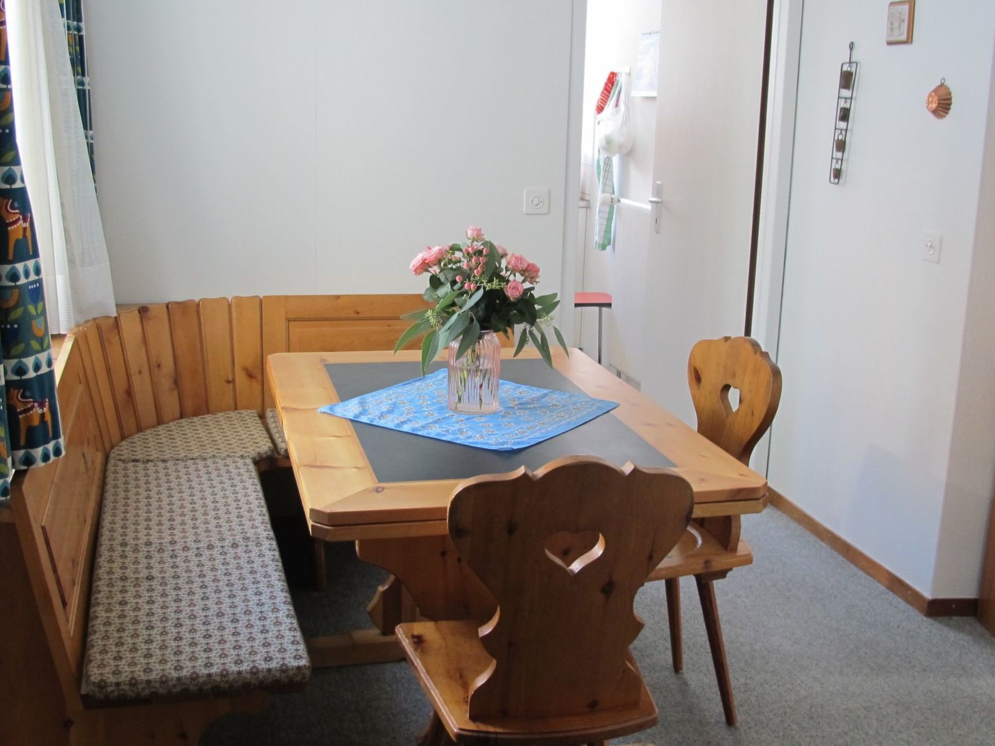 A dining area with a wooden table, bench seating, and a vase with flowers.