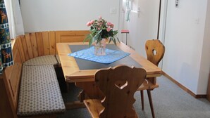 Un comedor con una mesa de madera, sillas, un banco y un florero con flores.