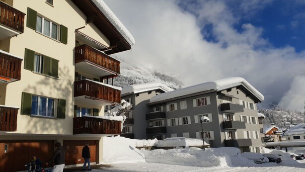 Un barrio residencial cubierto de nieve, con edificios de varios pisos, balcones y un cielo despejado.