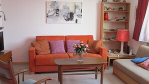 Una sala de estar con un sofá, una mesa de centro, una silla y una estantería.