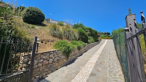 A stone pathway leading uphill, flanked by a stone wall and metal fence, with vegetation and a building in the background. - Casa Il Porticciolo di Rio Marina (Rio Marina)