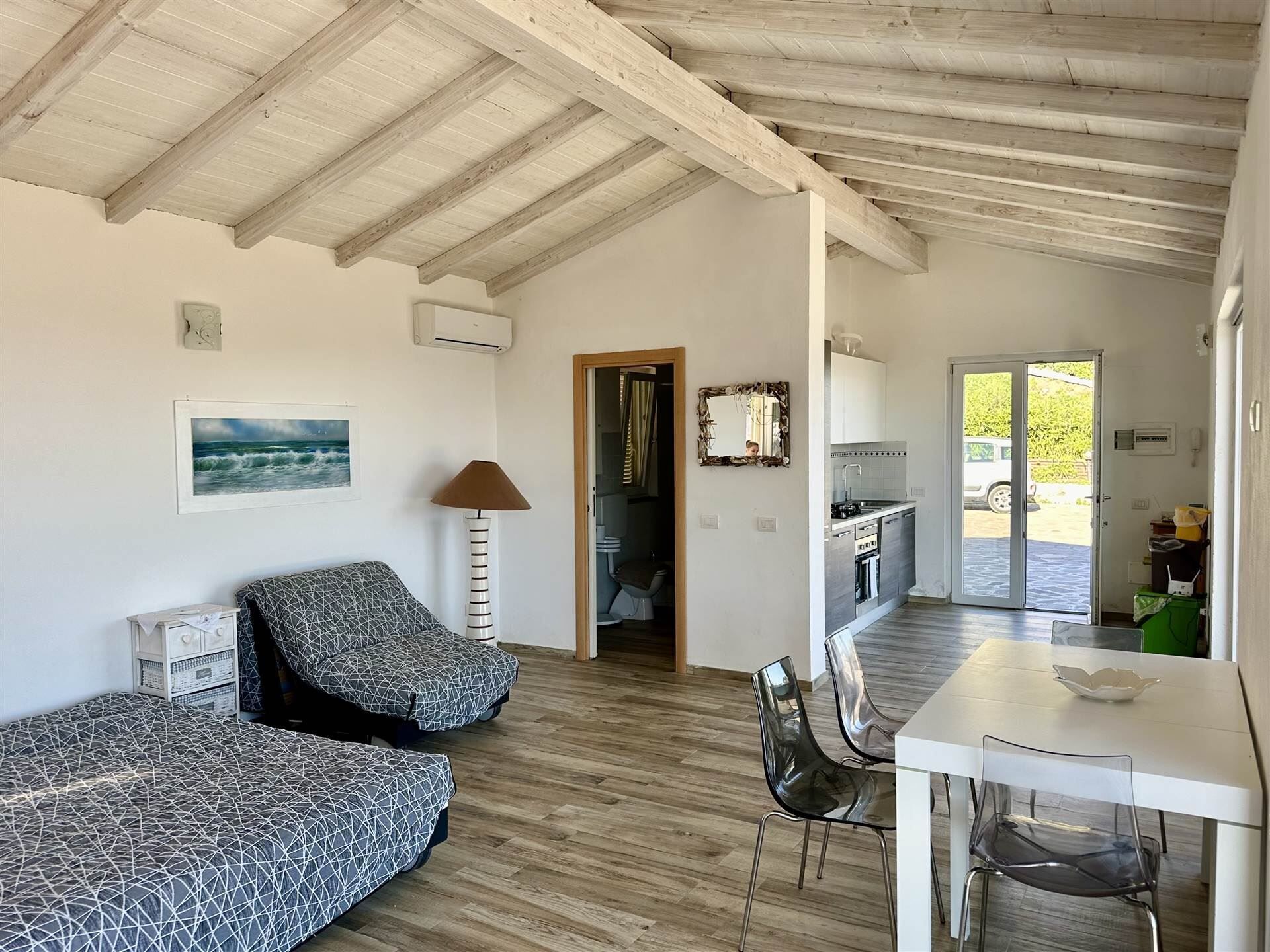 Un vaste espace de vie doté d’un haut plafond, une table à manger avec des chaises, un canapé et une cuisine visible à travers une porte ouverte.