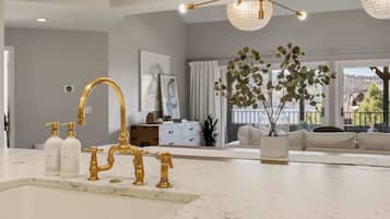 A modern kitchen with gold faucets, a marble countertop, and a view of the living area with a plant and a sofa.