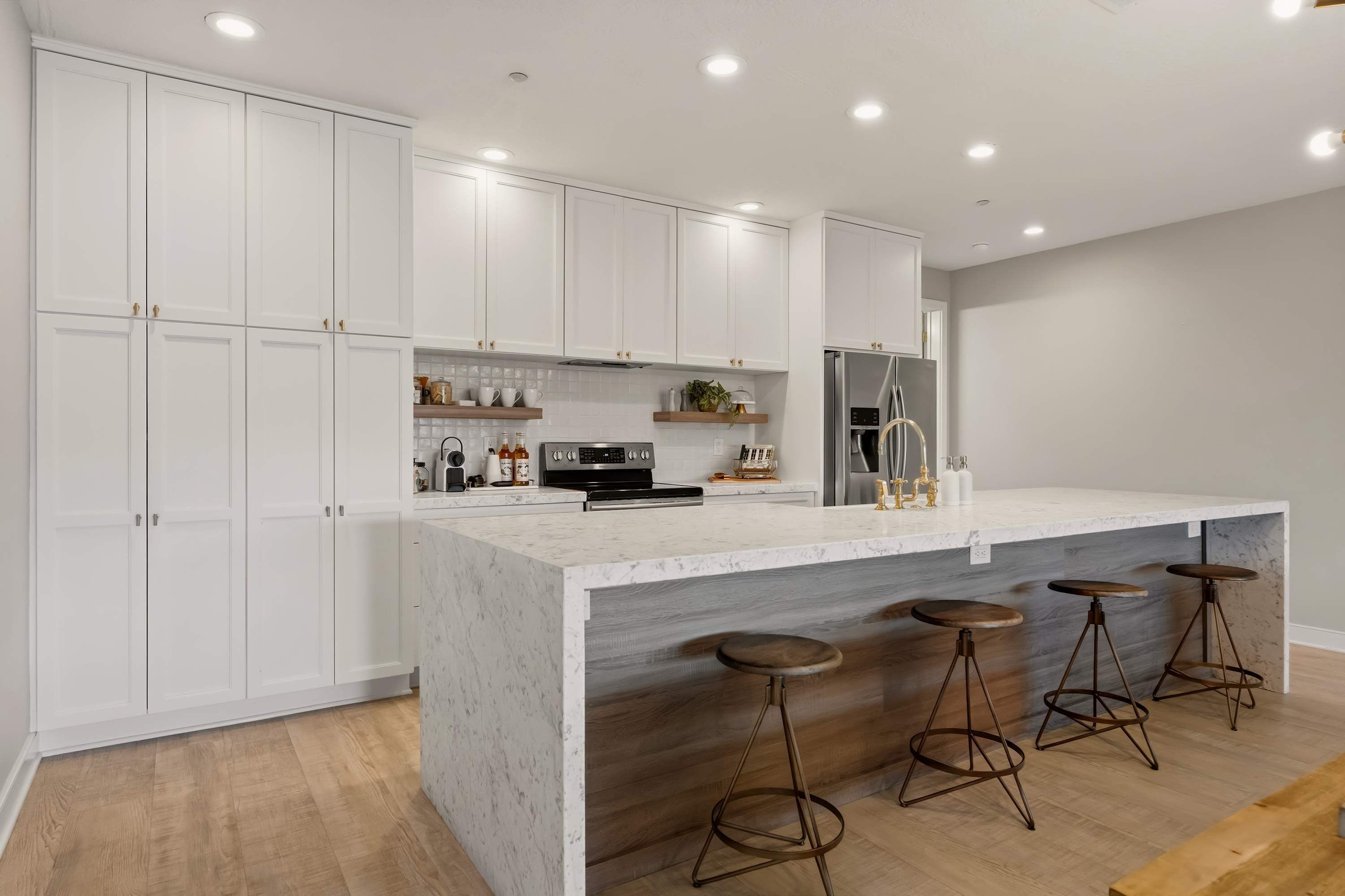 A modern kitchen with white cabinetry, a marble countertop, and a stainless steel refrigerator.