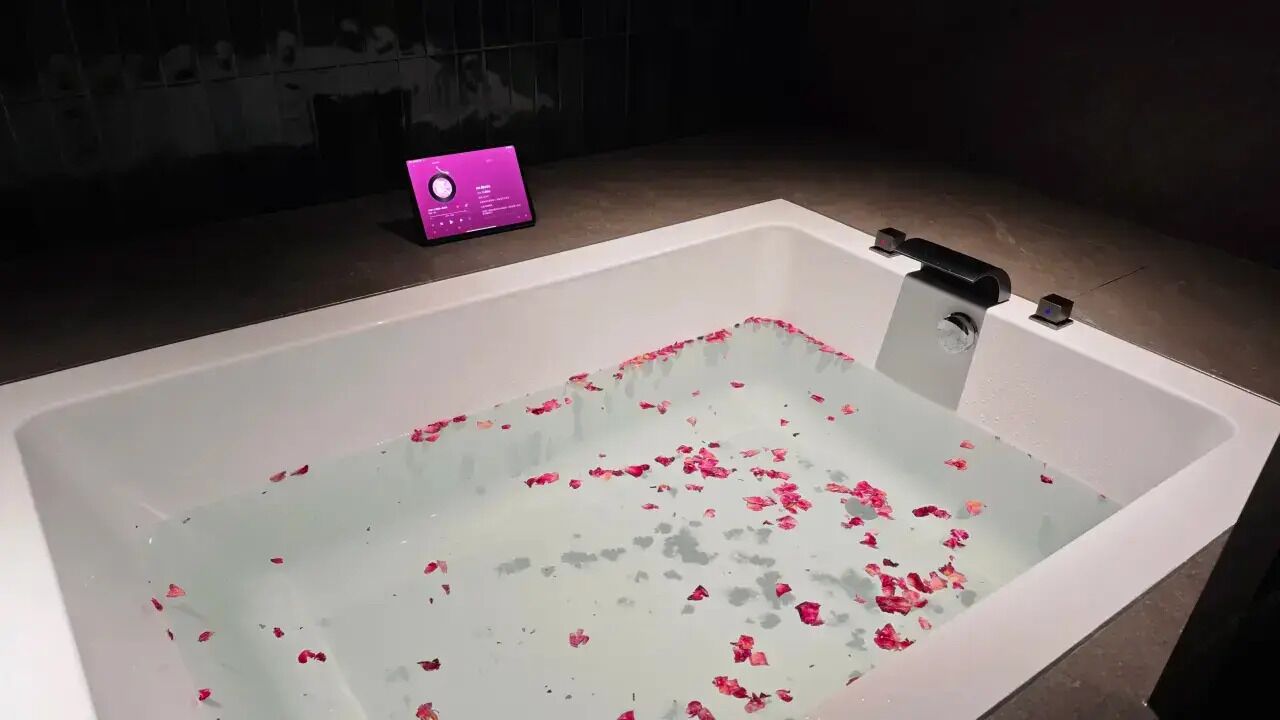 A bathtub with rose petals, a smartphone on the edge, and a dark background.