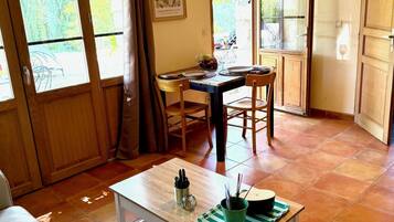 Un salon chaleureux avec un coin repas, des poutres apparentes, une table avec des chaises, un canapé et un luminaire suspendu.