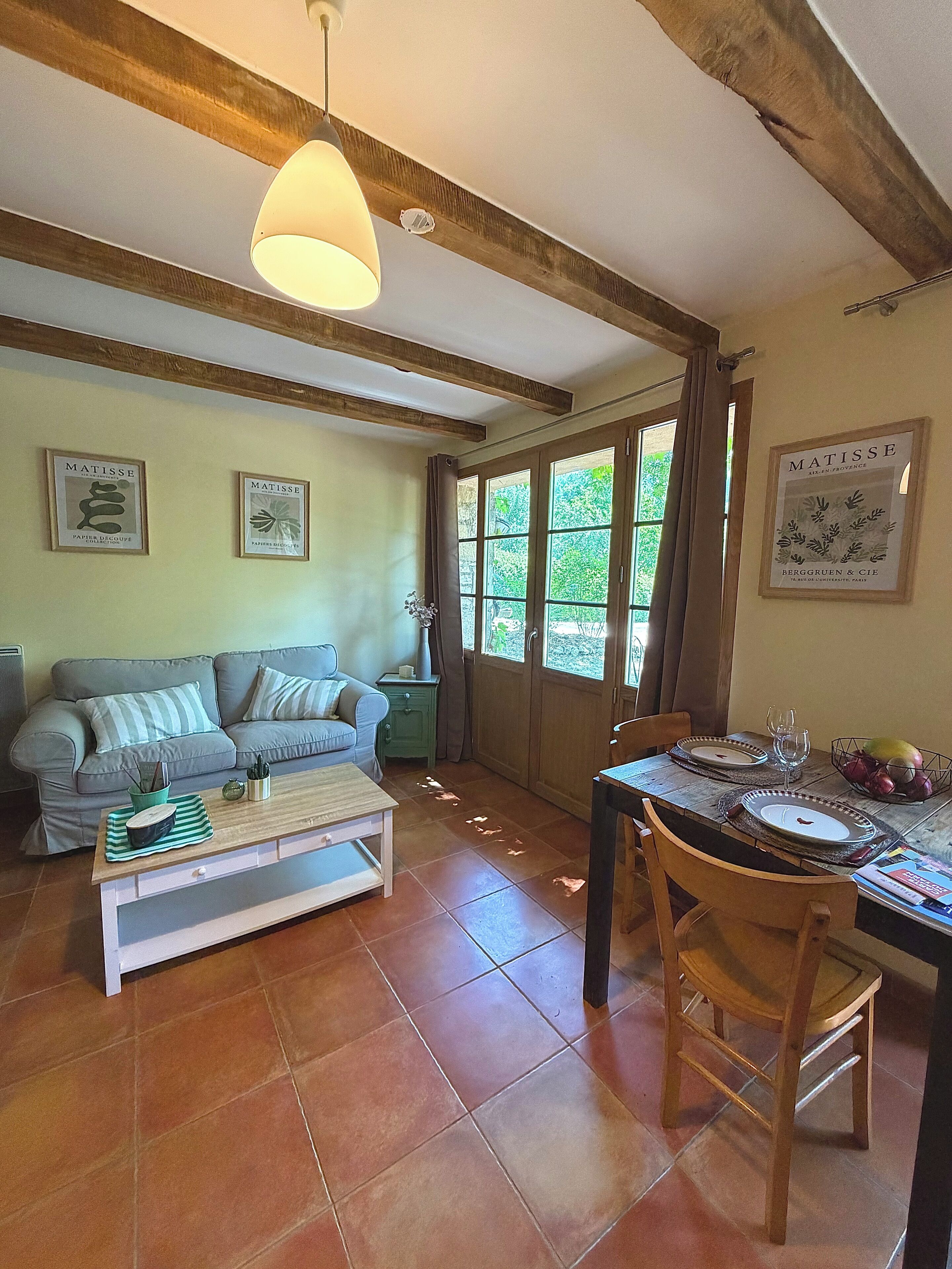 Un salon comprenant un canapé, une table basse, une table à manger dressée pour deux personnes et une fenêtre avec des rideaux.