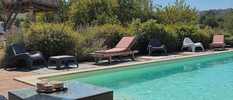 A poolside area with lounge chairs, a small table with a tray of items, and a wooden structure in the background.