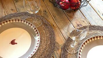 Una mesa de madera con una cesta de frutas, dos copas de vino y un plato con una flor roja.
