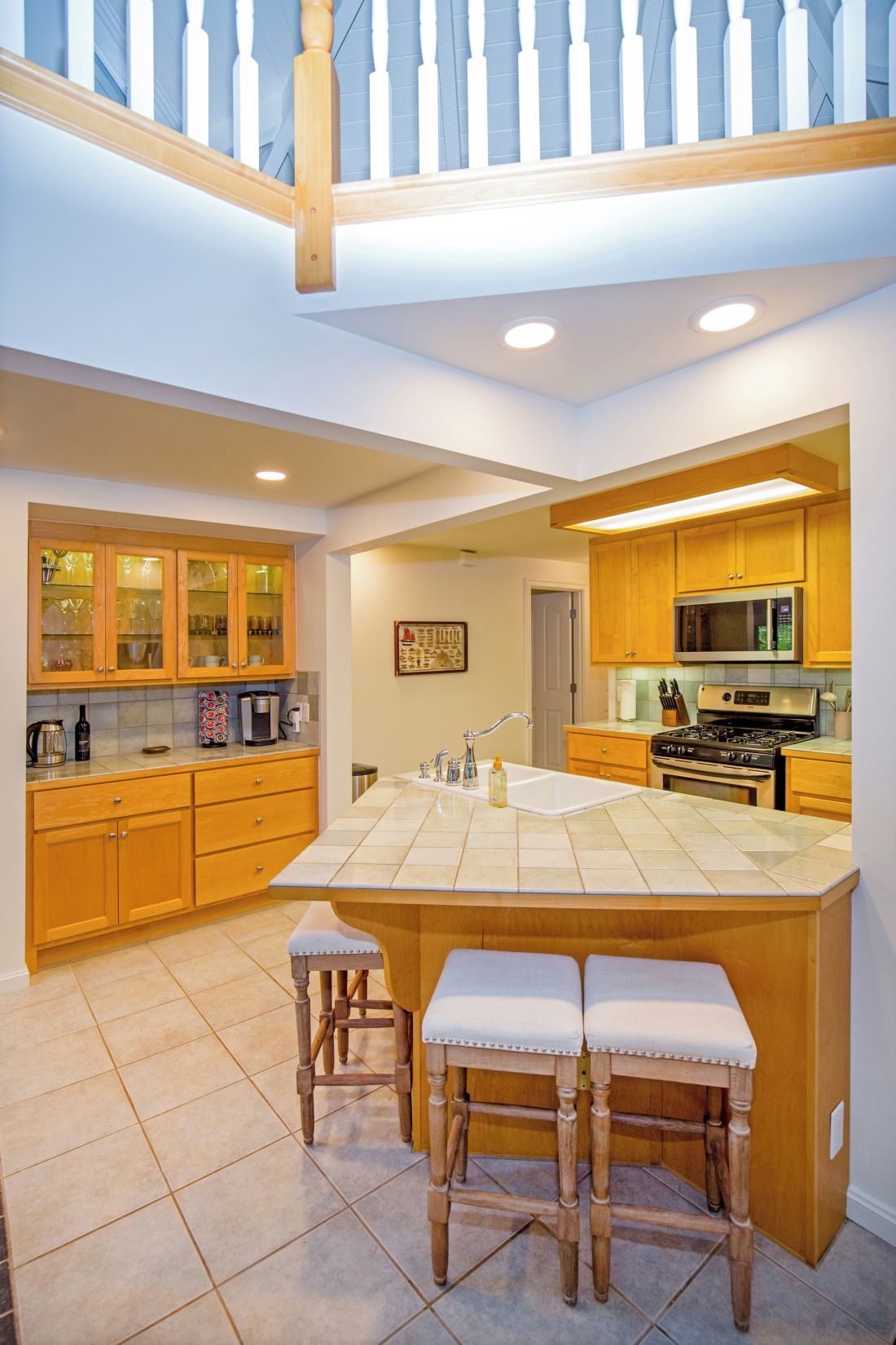 A modern kitchen with a central island, wooden cabinetry, and a staircase leading to an upper level.